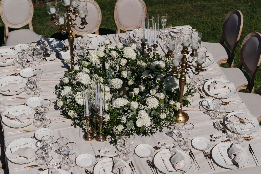 Weiß gedeckter Hochzeitstisch mit üppigem Blumenschmuck und goldenen Kerzenleuchtern