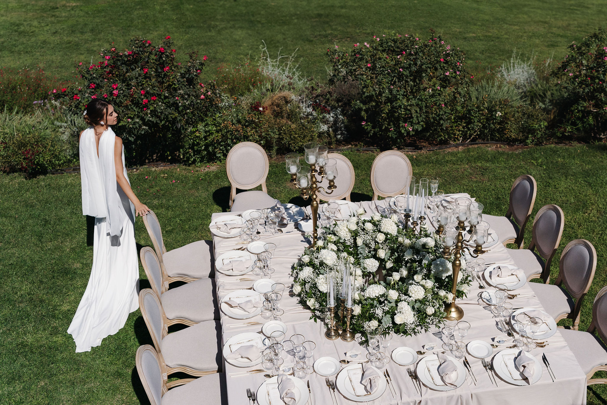 Braut neben der rechteckigen Hochzeitstafel mit weißer Floristik im Garten der Vigna Caio