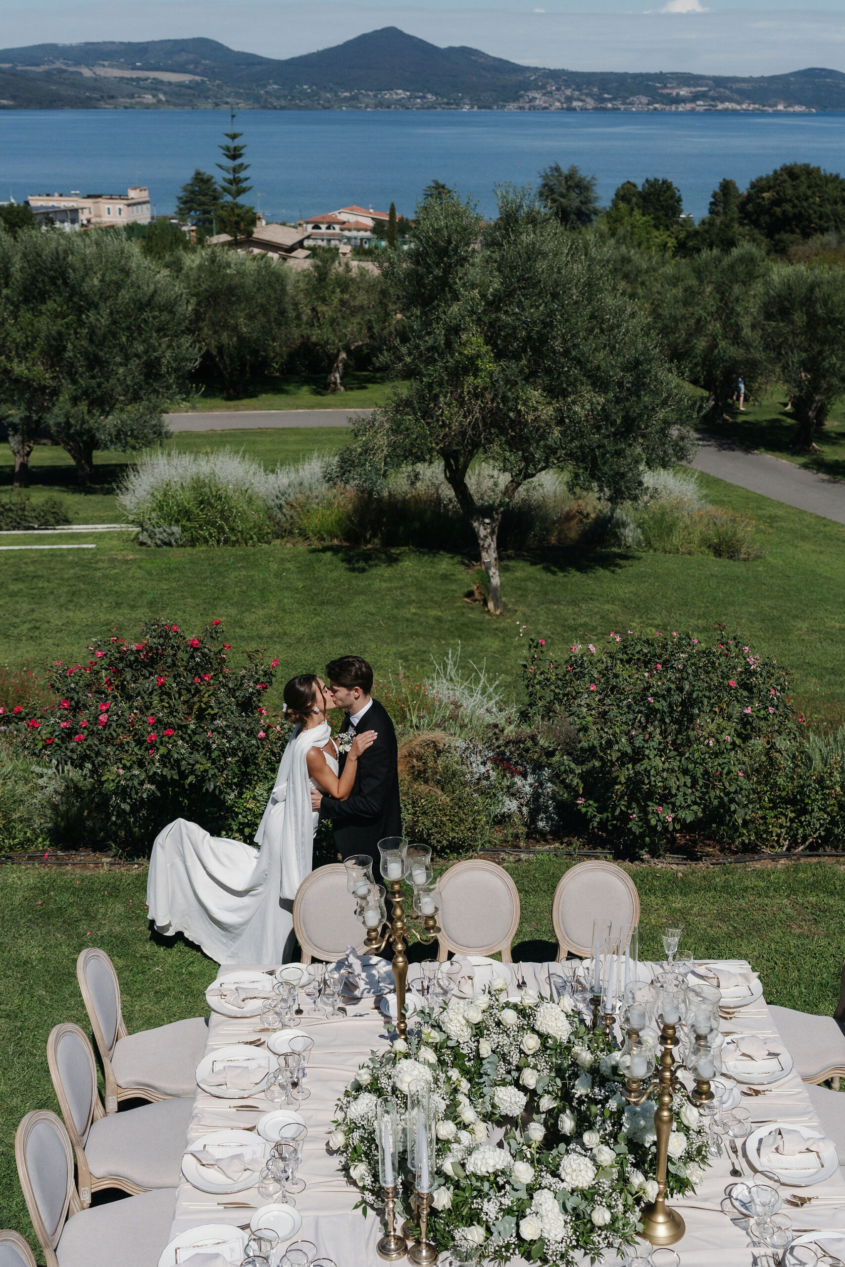 Brautpaar küsst sich neben der Hochzeitstafel mit Blick über den Garten zum Braccianosee