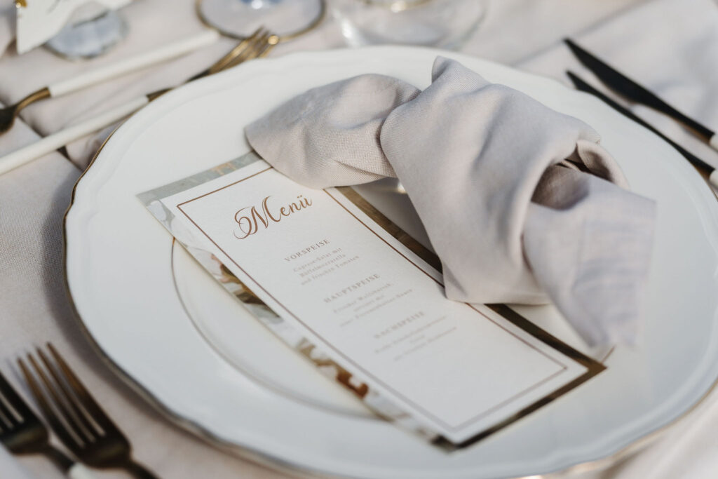 Menükarte mit goldener Schrift und champagnerfarbener Serviette auf weißem Teller