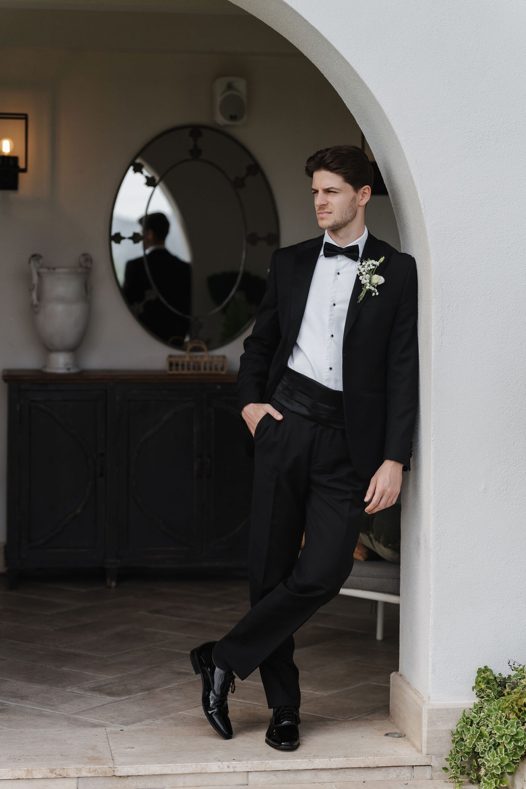 Bräutigam im schwarzen Hochzeitsanzug mit weißer Ansteckblume im Torbogen der Vigna Caio