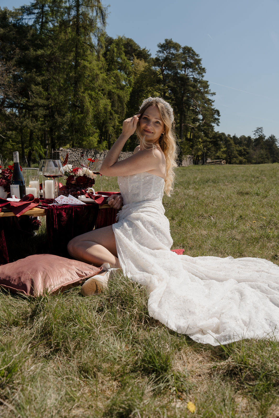 Braut sitzt im Hochzeitskleid am gedeckten Tisch auf der Wiese