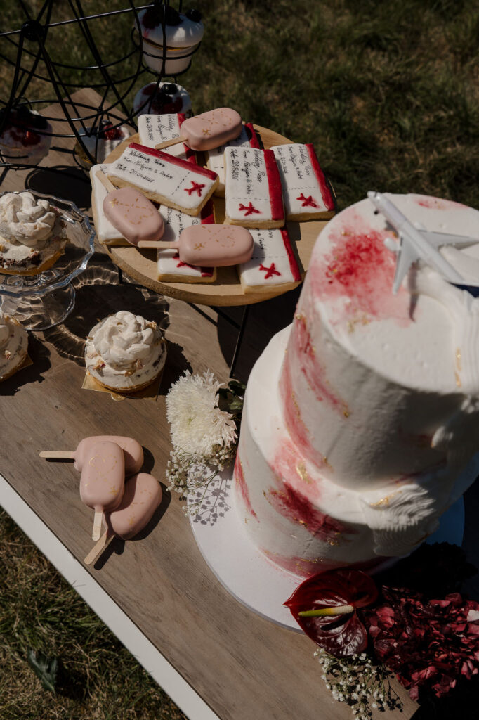Hochzeitstorte und rosa Dessertstücke auf einem dekorierten Tisch im Freien