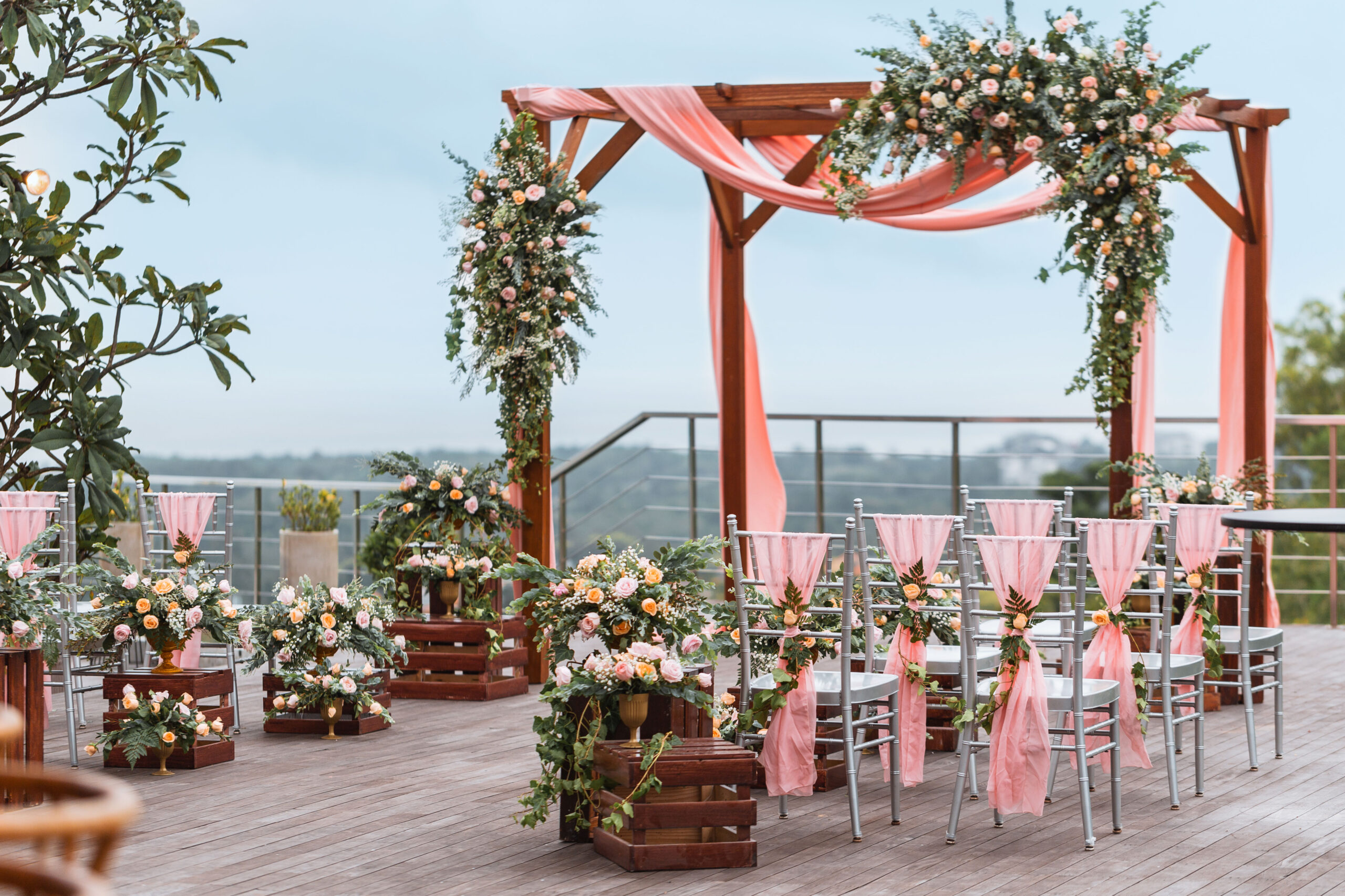 Hochzeitszeremonie mit rosa Drapierung, Blumenbogen und Stuhlreihen auf einer Terrasse